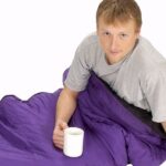Man still under his comforter while holding a cup of coffee