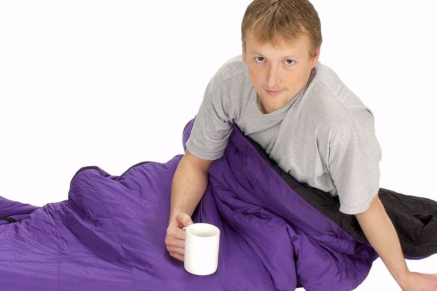 Man still under his comforter while holding a cup of coffee