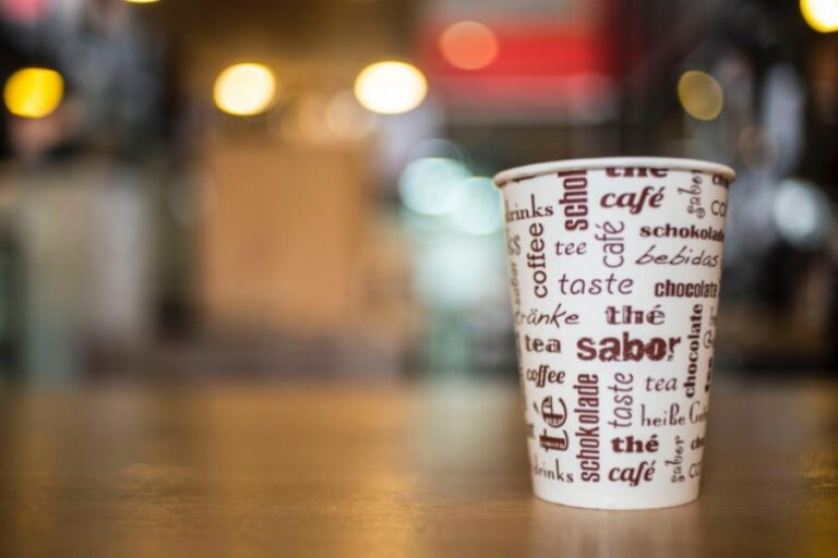 A white paper cup with printed materials was placed on a brown wooden table
