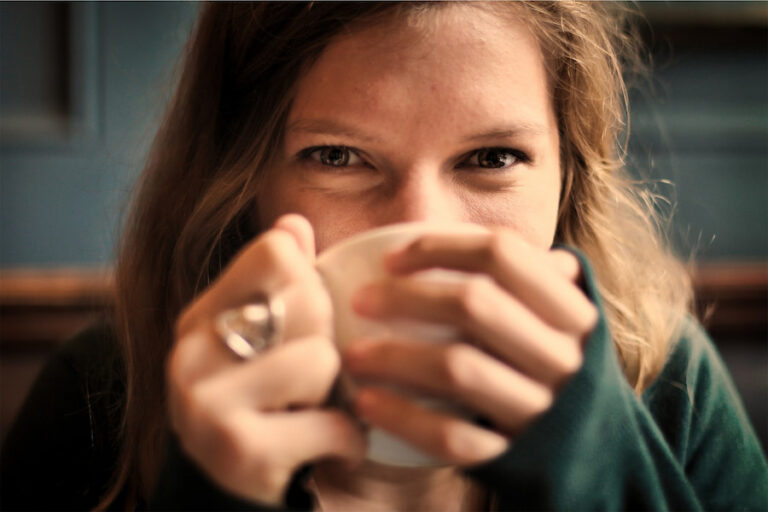 A woman wearing a green blazer and drinking coffee in a white mug in the apartment