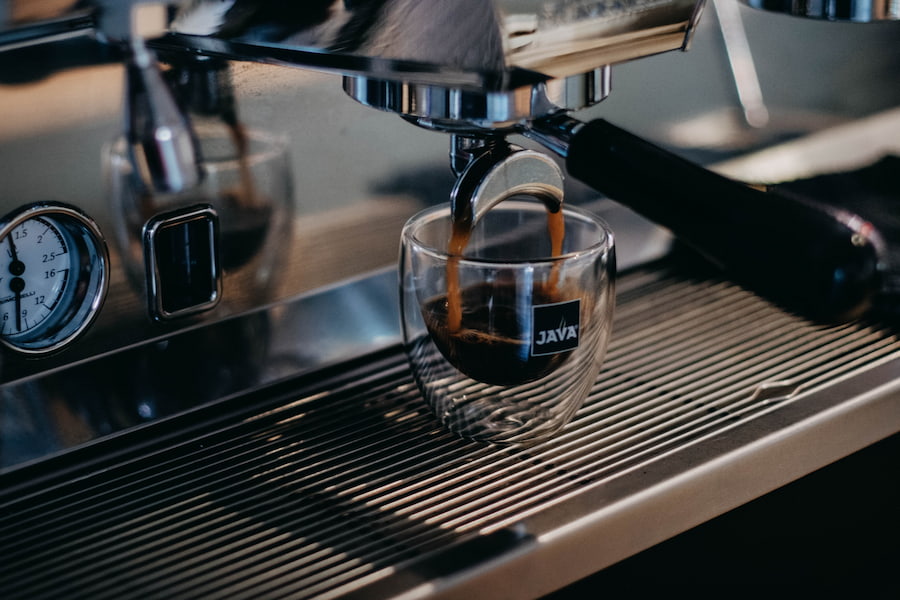 A silver espresso machine brewing an espresso shot in a small clear glass