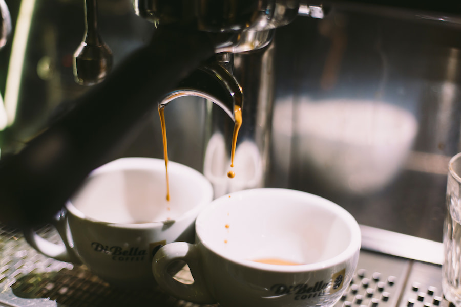 A silver espresso machine brewing into two small white cups placed on a silver surface