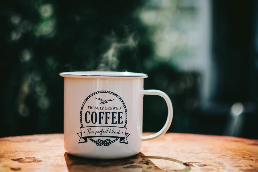 A white coffee mug with a black print placed on a brown wooden table