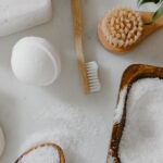 A wooden toothbrush surrounded by cleaning materials like soap and a brush placed on a white surface
