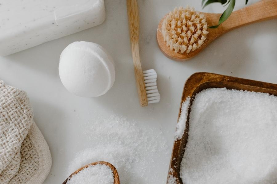 A wooden toothbrush surrounded by cleaning materials like soap and a brush placed on a white surface