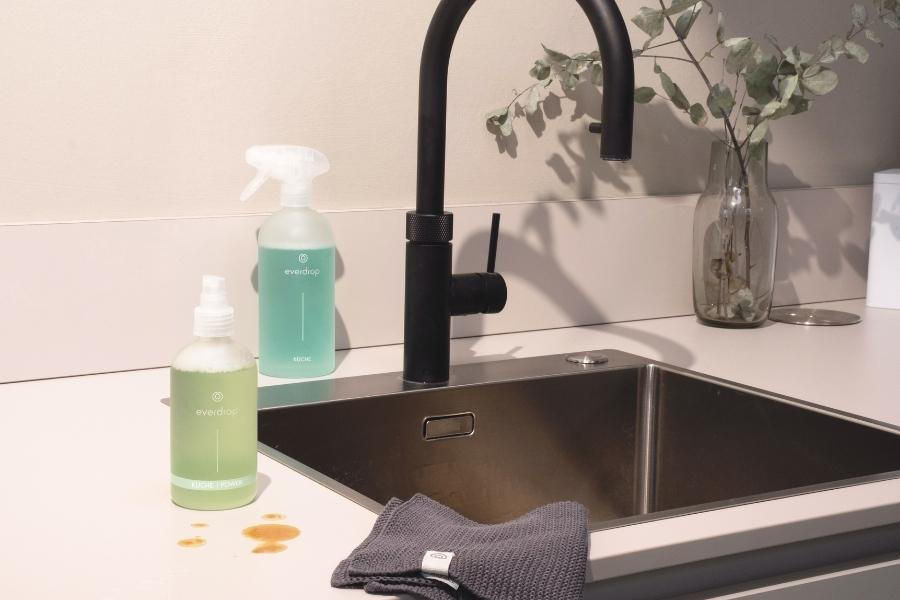 A stainless sink with a black faucet beside a spray bottle in the kitchen