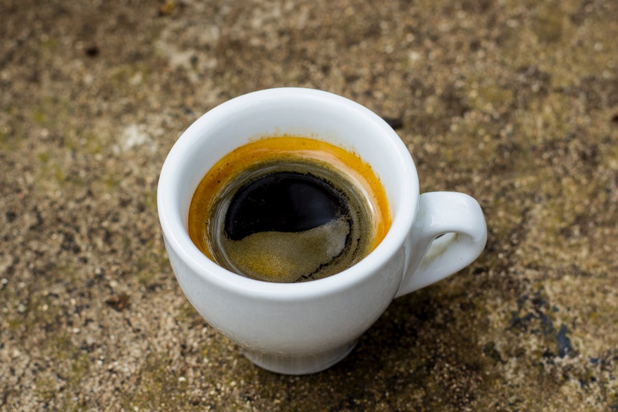 A white small cup with an espresso shot was placed on a granite floor