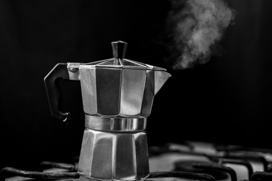 A silver stainless Moka pot with a black handle on top of a stove