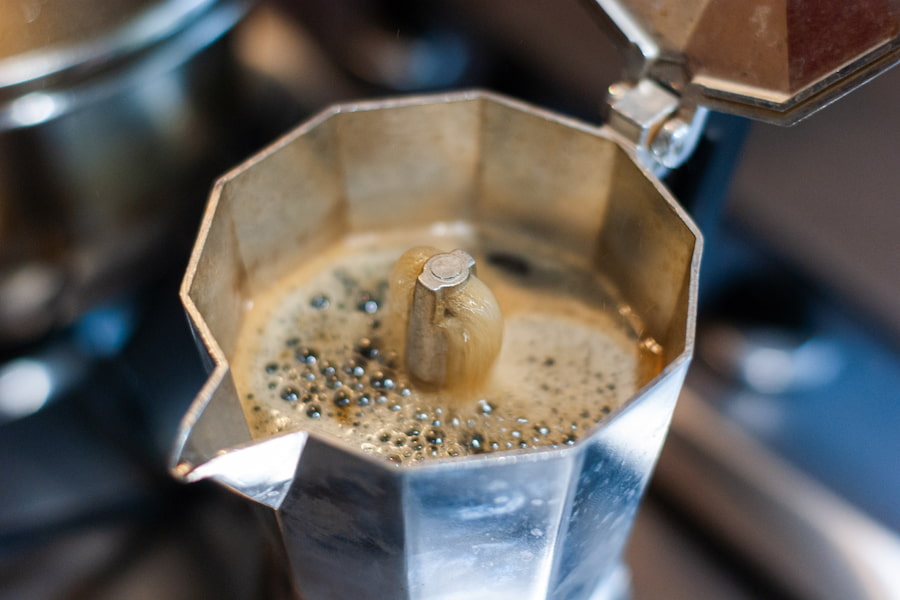 A close-up silver stainless Moka pot with a foamy coffee