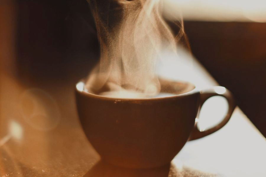 A white cup filled with hot coffee was placed on a brown wooden table in the kitchen