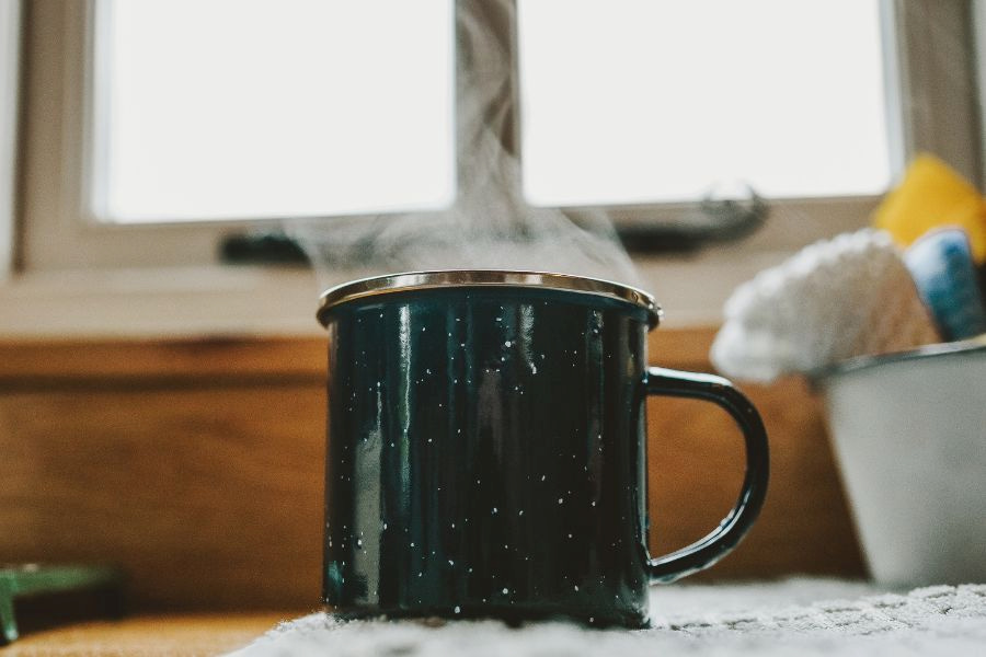 A green mug with a hot coffee was placed near a white window in an apartment