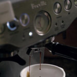 A close-up silver Breville coffee machine brewing a coffee in a white cup