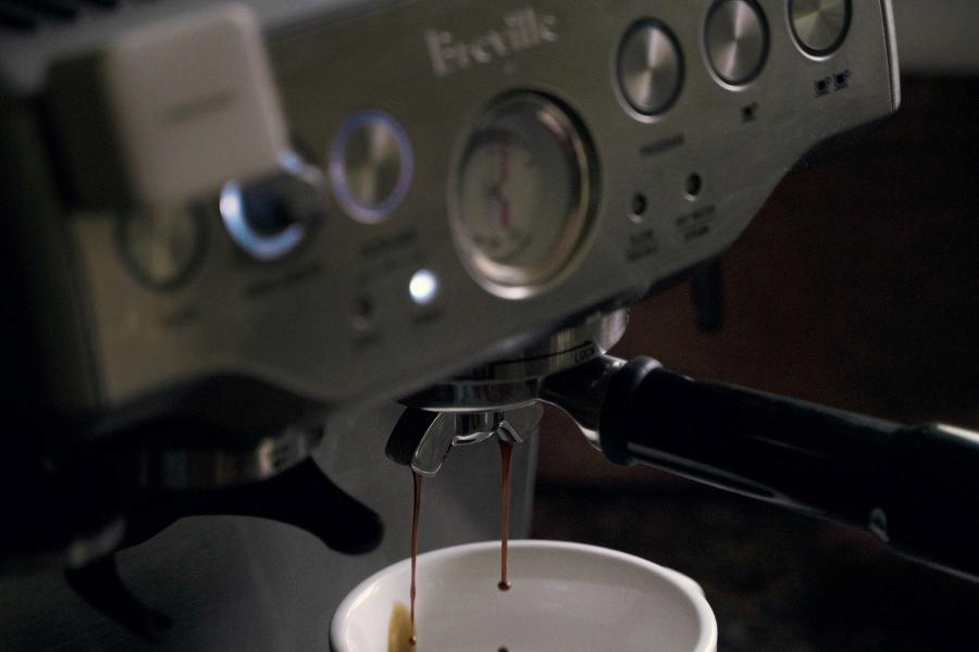 A close-up silver Breville coffee machine brewing a coffee in a white cup