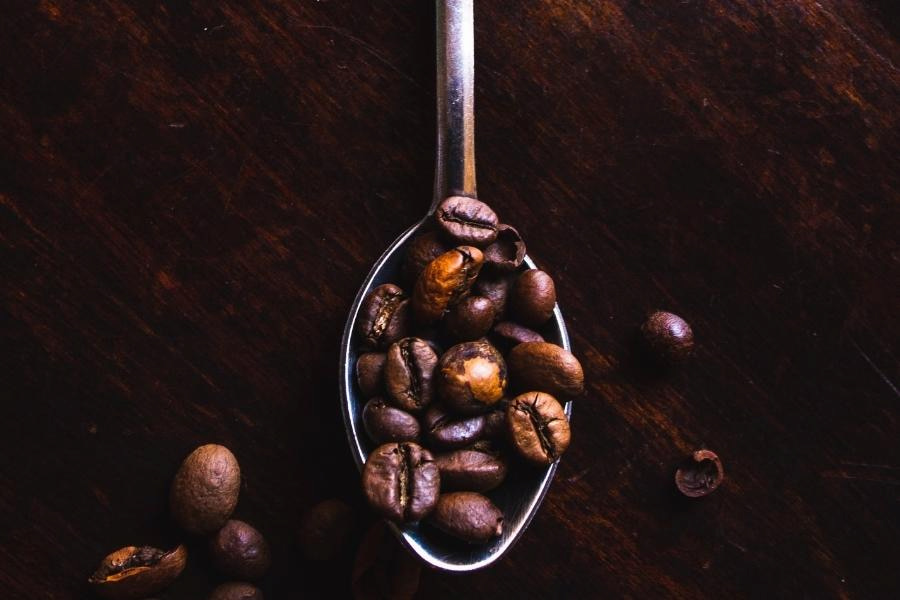 A silver spoon filled with fresh coffee beans was placed on a brown wooden table