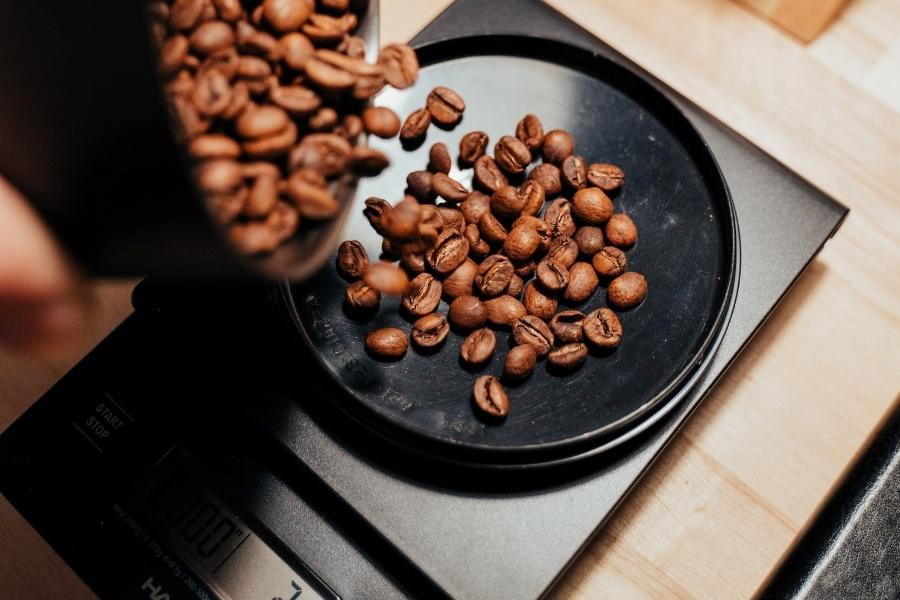 Fresh coffee beans weigh on a black weighing machine placed on a brown table