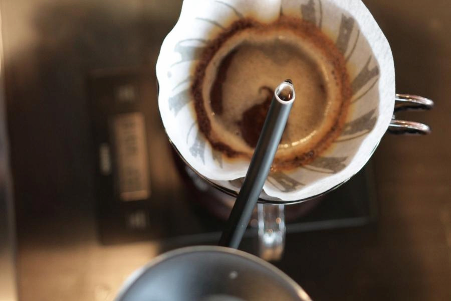 A close-up black pour-over coffee kettle is used in a silver pour-over coffee maker placed on a black surface