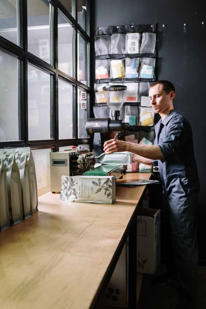 A man in a blue long-sleeved shirt and blue pants holds a white pouch bag of coffee in the shop