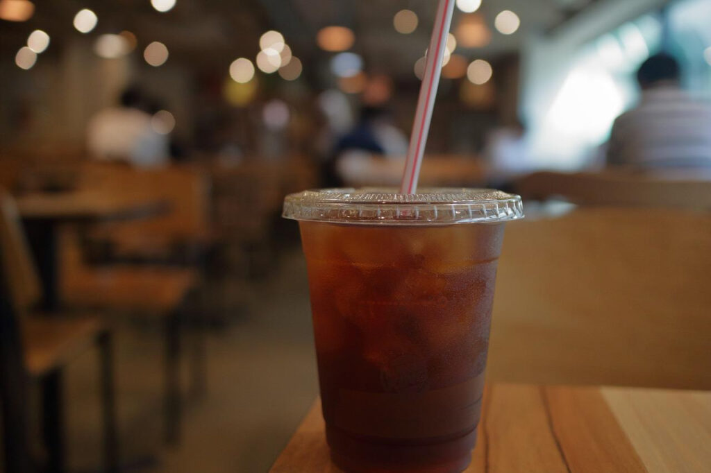 Ice cold coffee in a plastic cup with a straw on top of a brown wooden table in a coffee shop