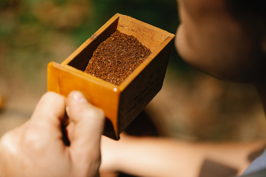 A person holds a small brown wooden box with a coffee ground in it