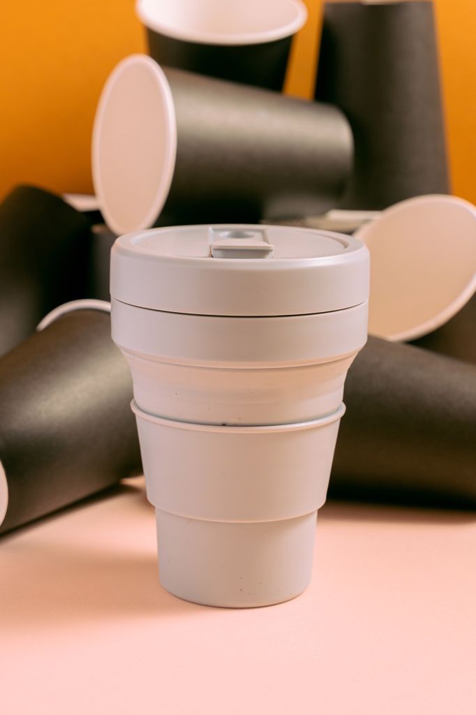 One white reusable cup and many black plastic cups are placed on a pink surface