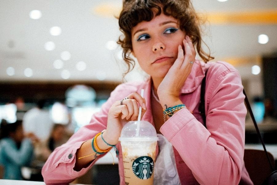 A woman in pink long sleeves drinks an iced coffee from Starbucks in the shop