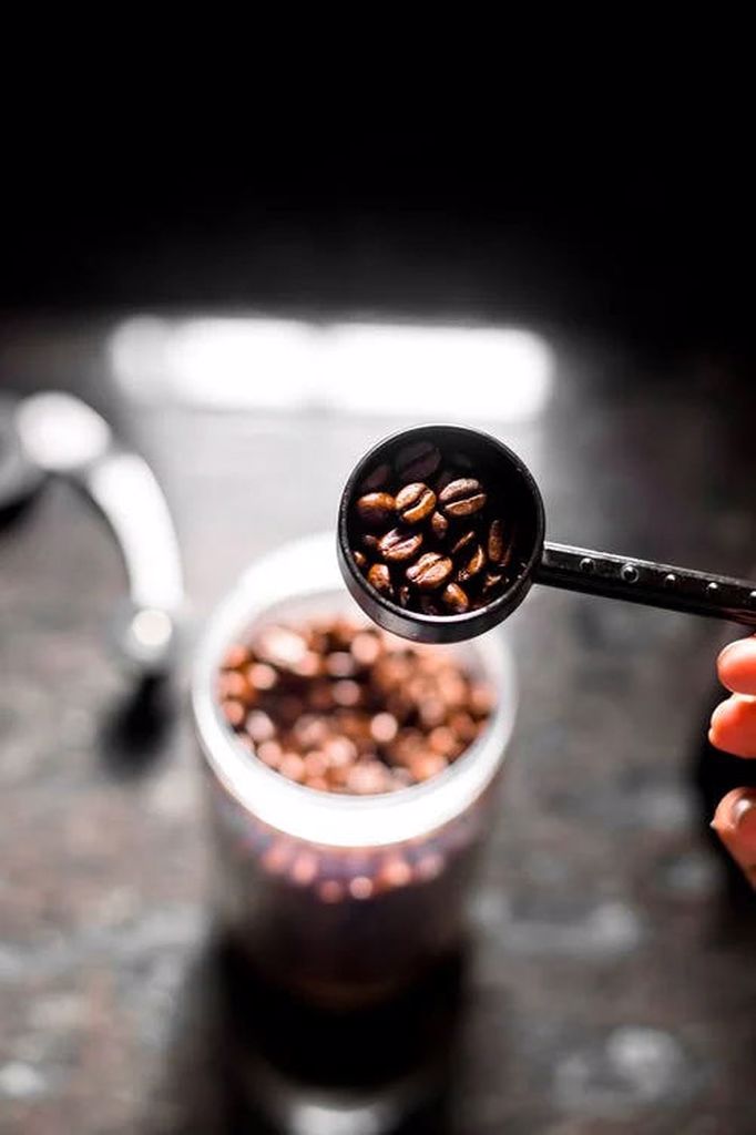 A person holds a black coffee scoop full of fresh coffee beans