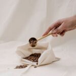 Hand holding a scoop full of coffee beans placed on a white cloth bag