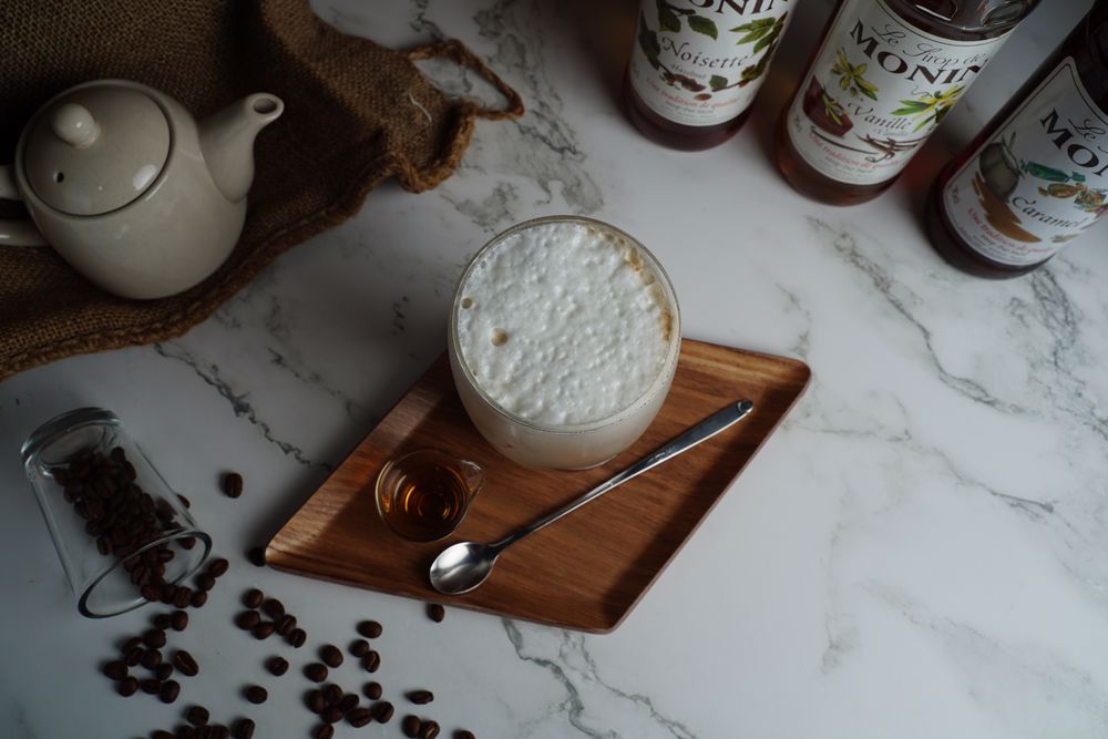 Fresh coffee beans tipped over clear glass with a glass of coffee frappe beside it