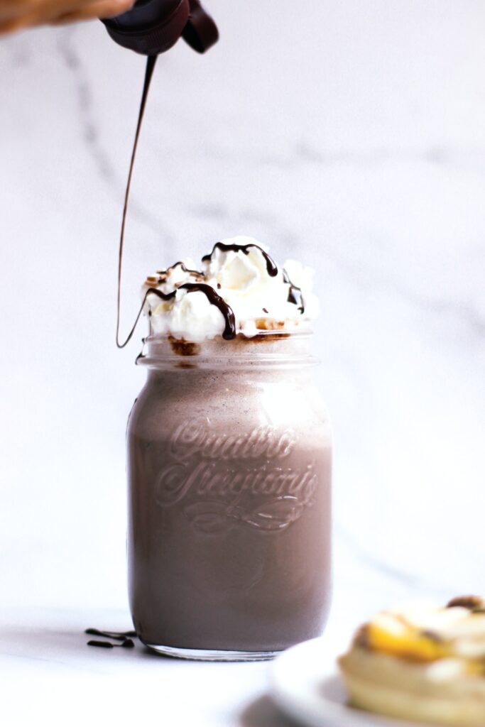 A frappuccino with whipped cream drizzled with chocolate syrup in a mason jar placed on a white surface