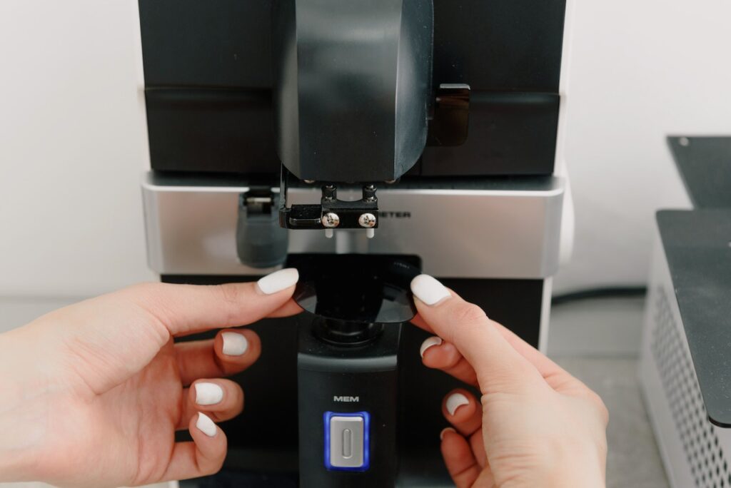 A hand of person with white nail polish fixes a black and silver coffee machine in the kitchen