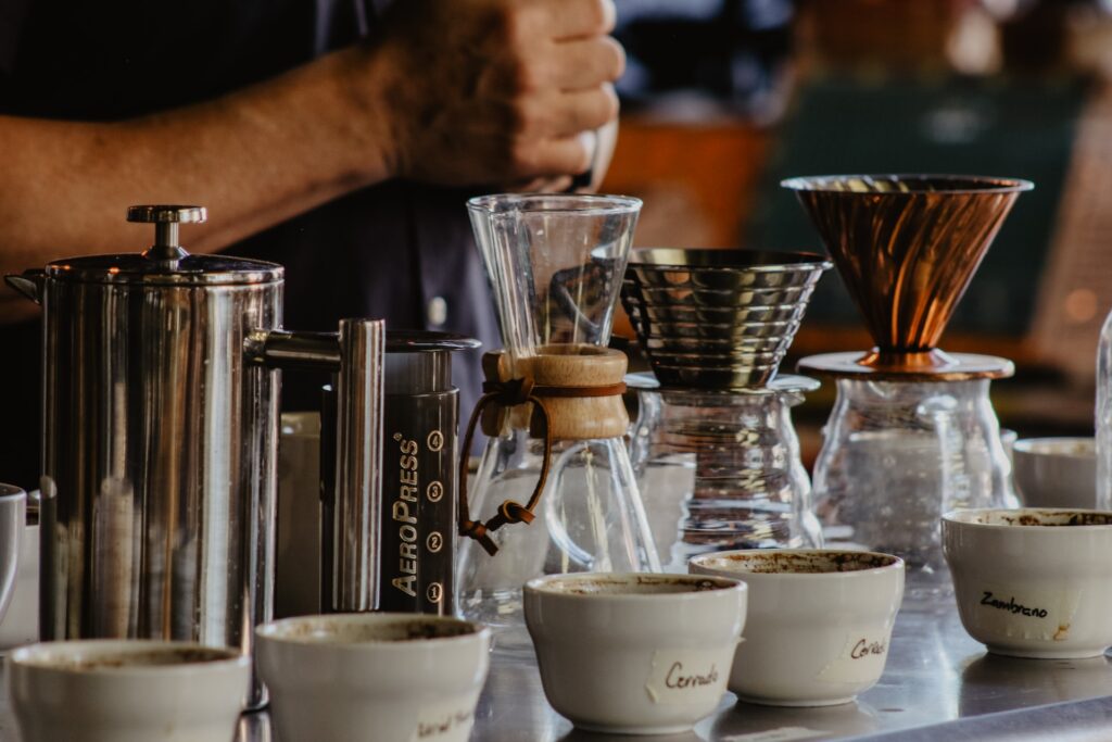 A person stands in front of the different types of coffee makers and white bowls on top of a stainless table