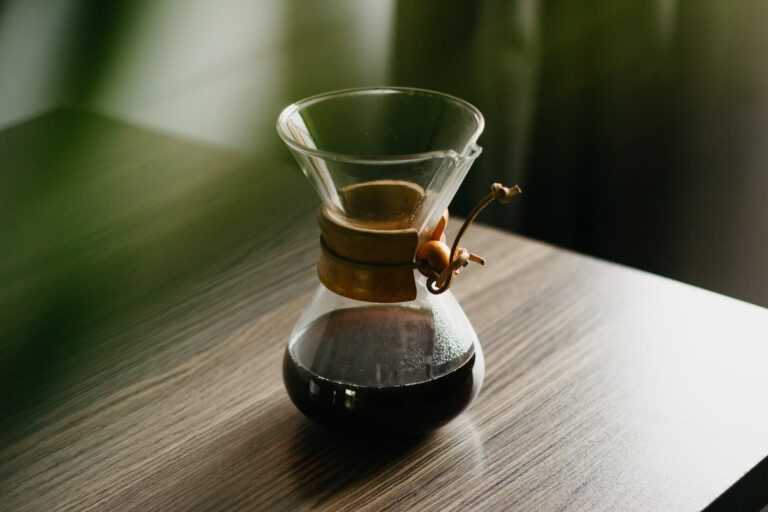 Chemex pour-over glass coffeemaker with a natural wood collar on top of a brown wooden table