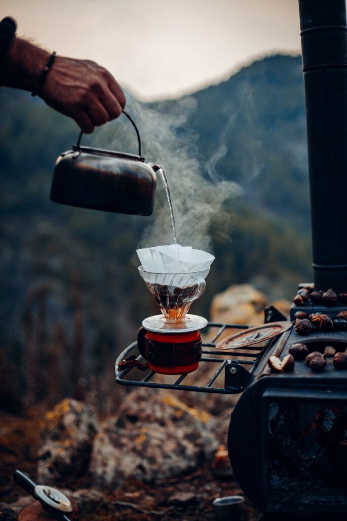 Hot water is placed in a stainless kettle being poured into a red and black cup