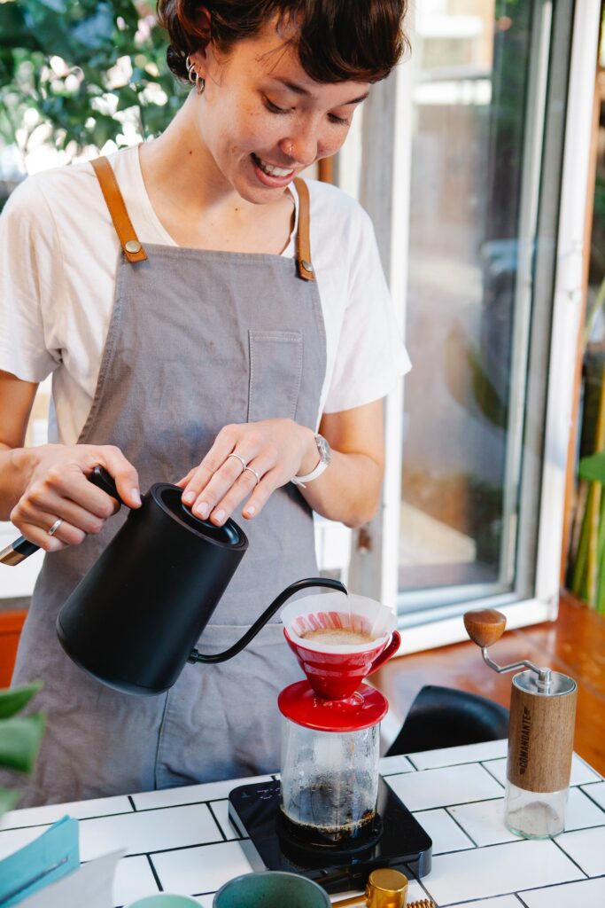 A black stainless electric kettle used by a happy young woman in pouring hot water to make a coffee