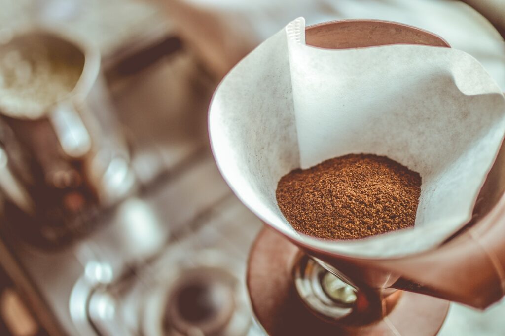 Brown coffee grounds on a white filter paper on a brown mug near a gas stove