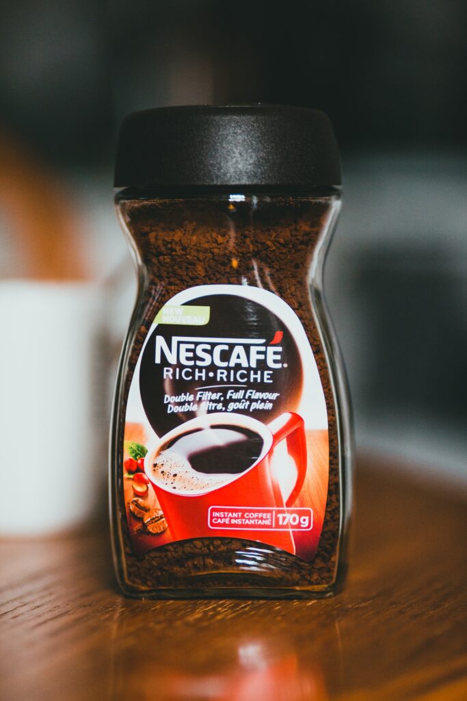 A full Nescafe instant coffee in a glass container with a black lid on a brown wooden table
