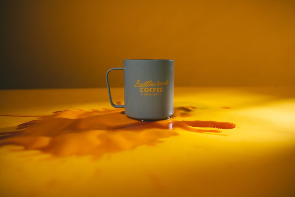 A coffee spilled from a coffee mug was placed on top of a yellow table inside a room