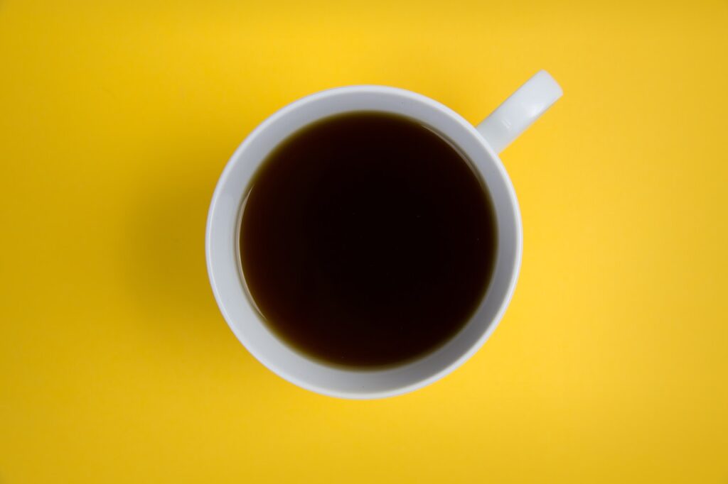 Black coffee on a white mug placed on top of a yellow surface