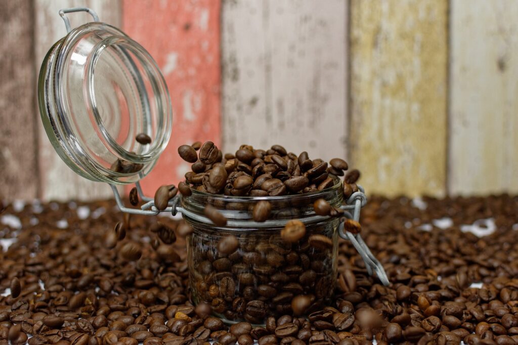 A clear mason jar filled with coffee beans on top of roasted coffee beans near a colorful wooden fence