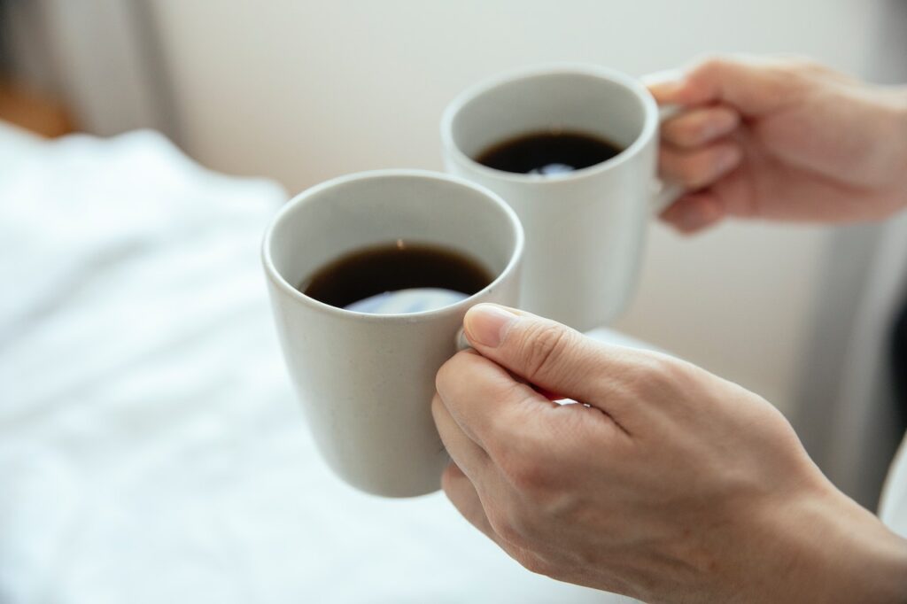 A person's hands holding two white mugs filled with black coffee in the kitchen
