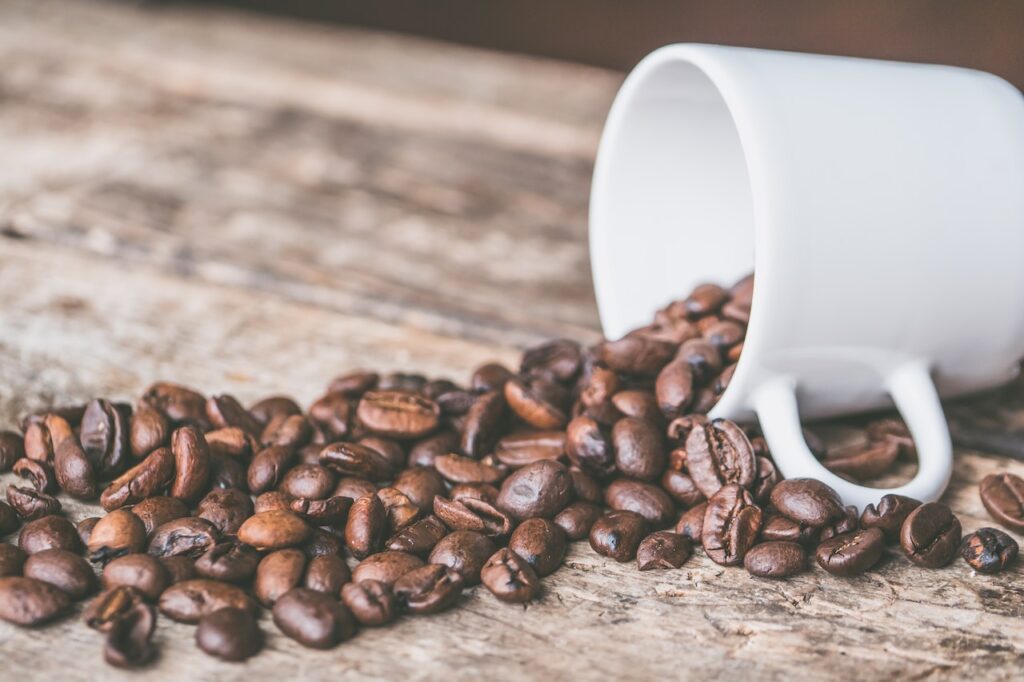 Fresh whole coffee beans spilled from a white coffee cup were placed on a brown wooden table