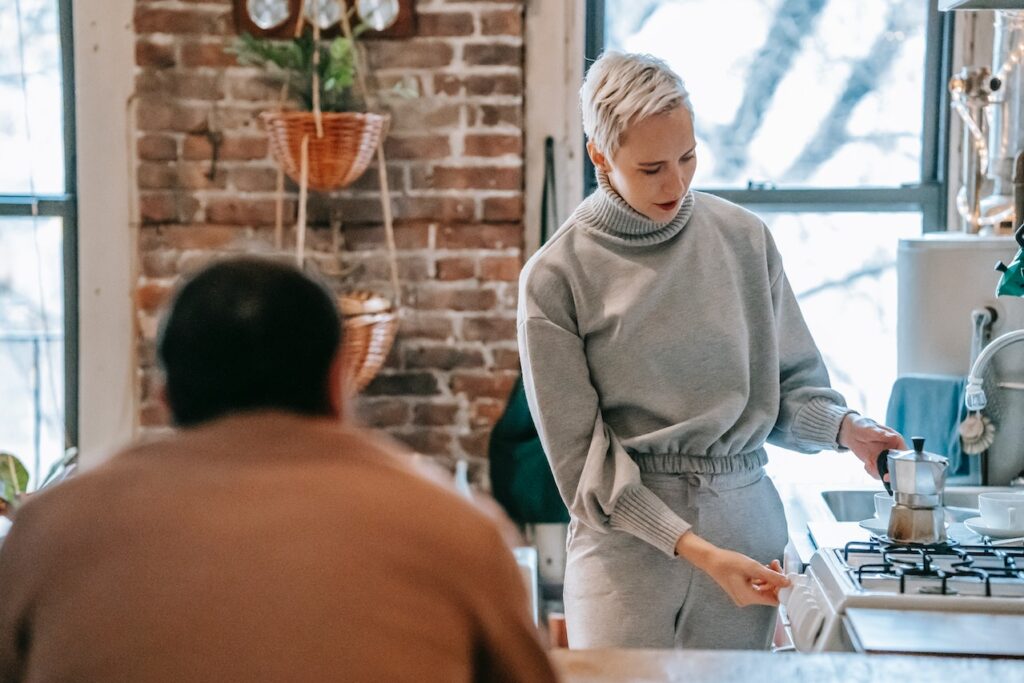 A woman in a gray sweatshirt and gray sweatpants using a silver Moka pot to brew a coffee on a stovetop