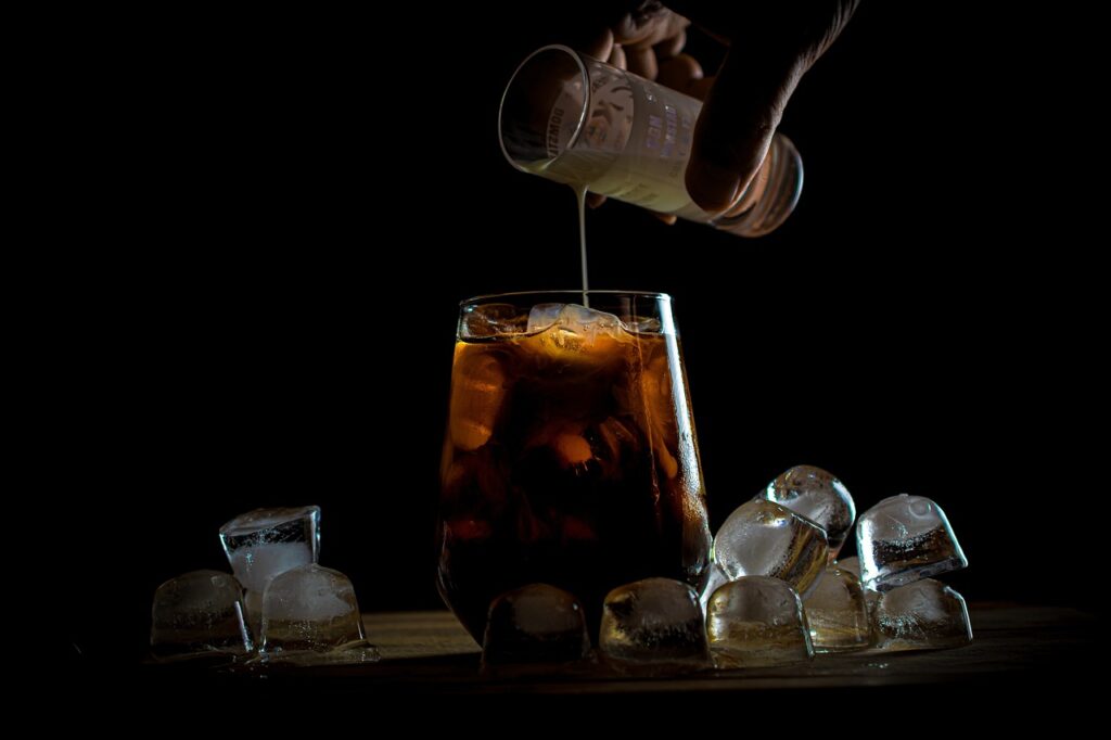 A person adding milk to iced cold coffee placed on a glass