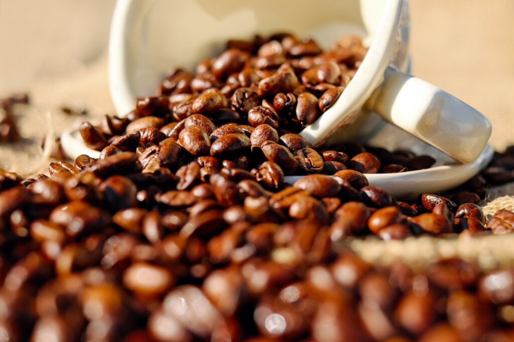 Close-up fresh coffee beans and a white cup of coffee half-filled with coffee beans