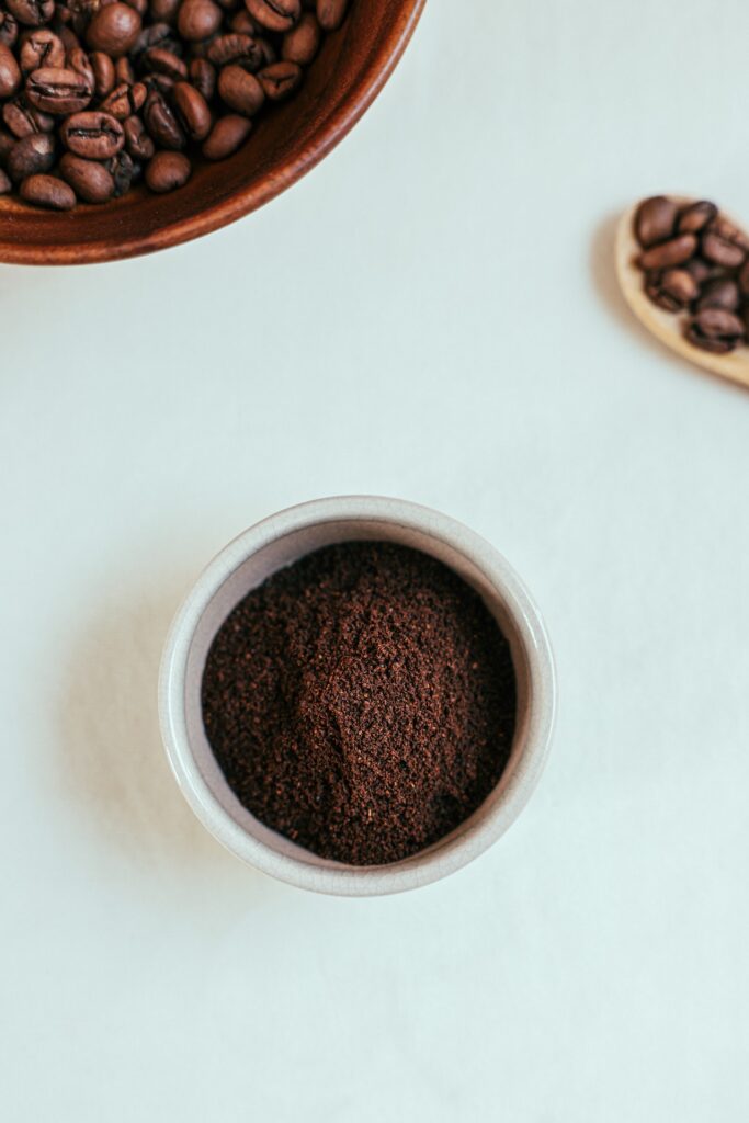 Grind coffee in a white bowl and whole coffee beans in a brown bowl placed on a white surface