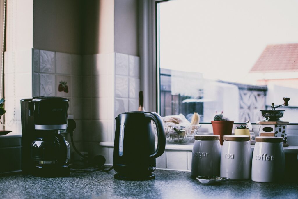 A black coffee maker on a marbled table near a tiled wall