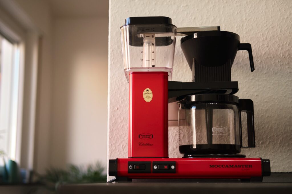 A red and black coffee maker on a black table near a white wall