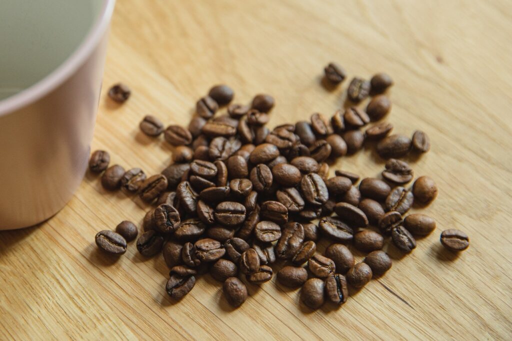 Coffee beans beside a pink mug on a brown wooden table