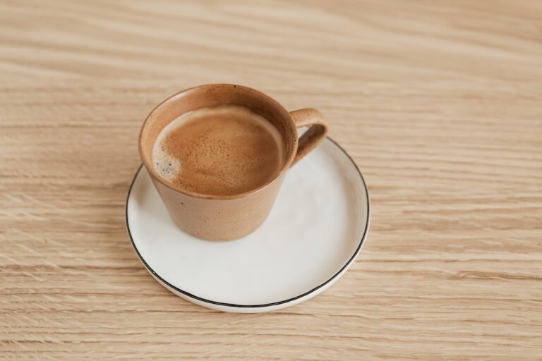 A cup of coffee in a brown mug placed on a white saucer