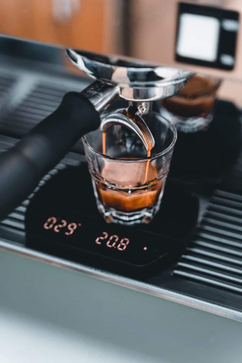 A close-up of an espresso placed on a shot glass being extracted from a coffee machine